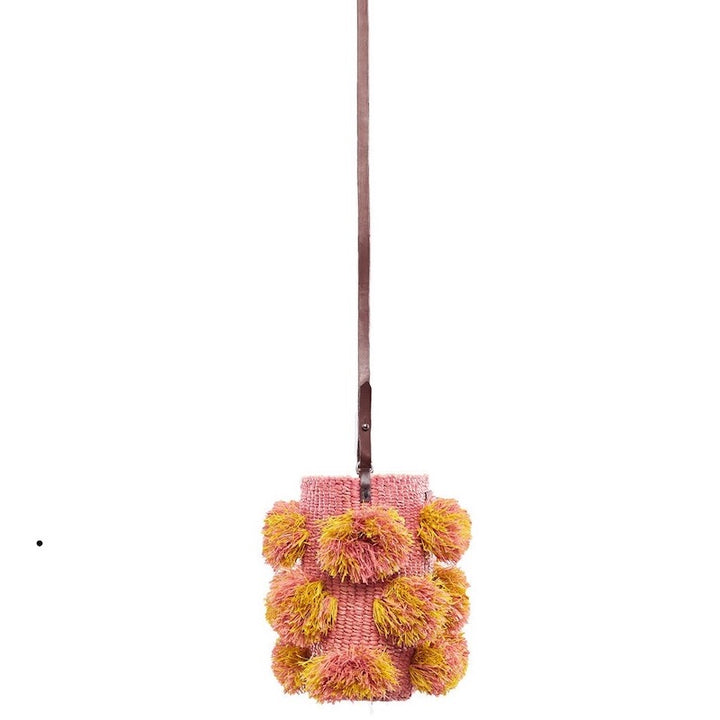 side view of a raffia pompom bag with an all over fringe detailing in soft pink and yellow colors and 39" leather strap drop