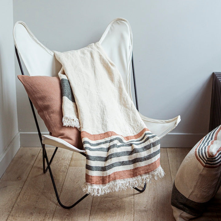 100% Belgian linen throw on a butterfly chair. The throw can be worn or used as a blanket. It's heavy natural cream tone with dark olive green and red earth stripes