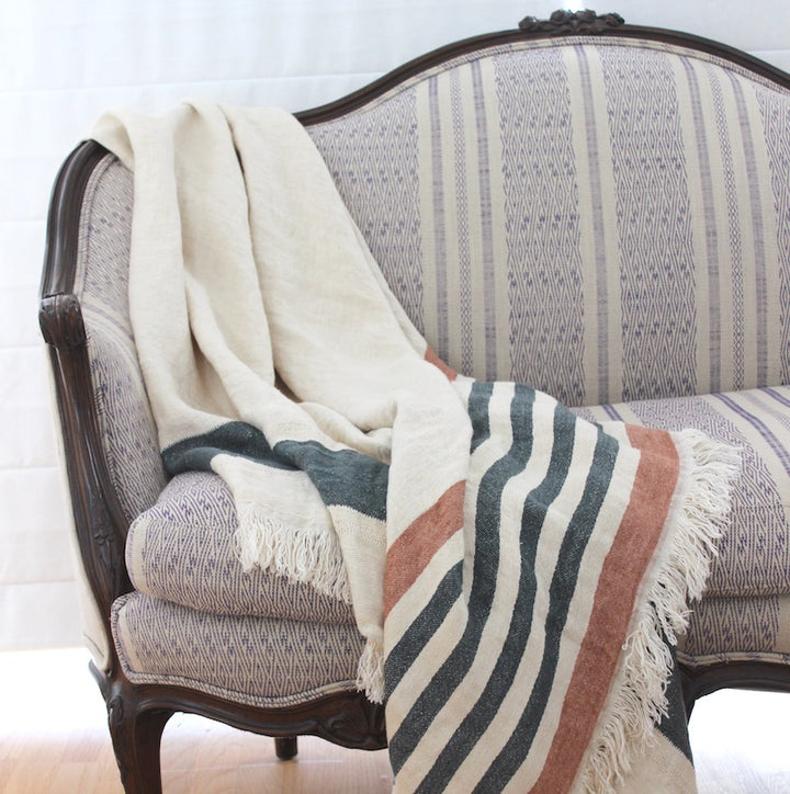 100% Belgian linen throw on a chic love couch. The throw can be worn or used as a blanket. It's heavy natural cream tone with dark olive green and red earth stripes