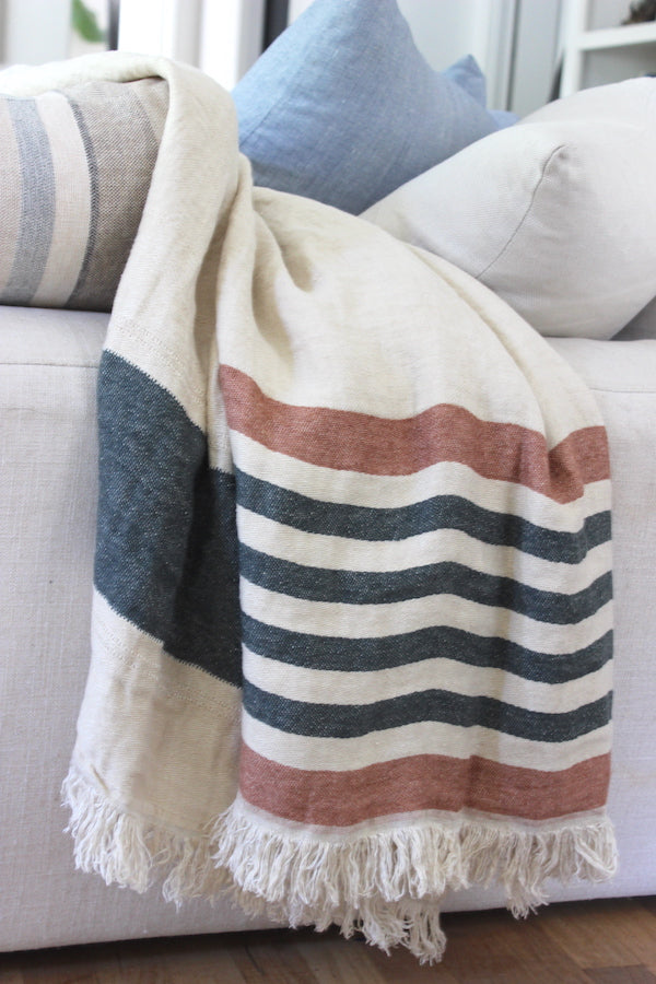 100% Belgian linen throw on a comfy couch. between the lush pillows. The throw can be worn or used as a blanket. It's heavy natural cream tone with dark olive green and red earth stripes