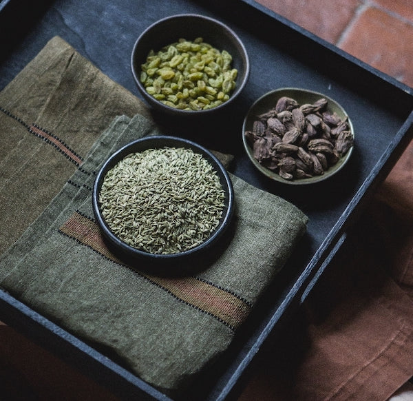 A tray of interesting seeds with Libeco Belgian linen napkins, Marie; One end of this open weave constructed olive green napkin is featuring black stitchings across in two lines juxtaposed by orange band on the other side.