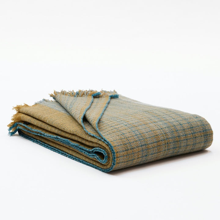 Folded blanket in 100% Merino wool. Llghtweight, flat woven pieces made with 100% pure Merino wool woven in 5 shades of olive green & turquoise colors